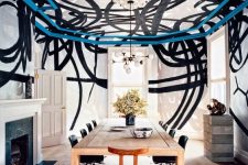a chic modern dining room with a black and white graffiti ceiling and walls, a stained table, black chairs, a fireplace with a black marble surround