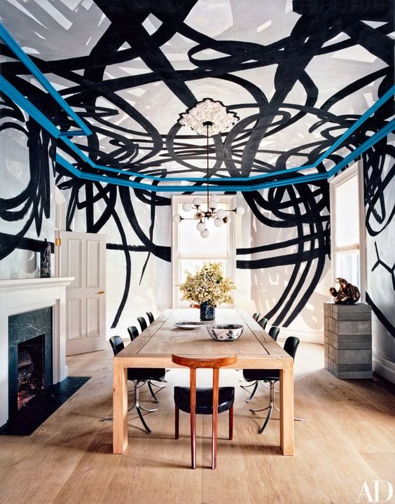 a chic modern dining room with a black and white graffiti ceiling and walls, a stained table, black chairs, a fireplace with a black marble surround