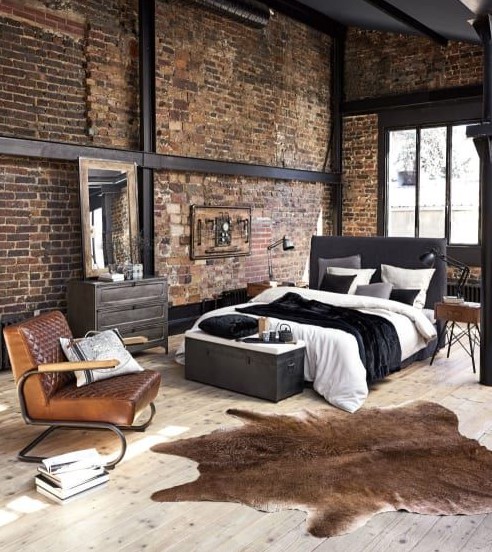 a chic modern industrial bedroom with exposed metal, brick walls, upholstered furniture, a chest for storage and some animal skin rugs