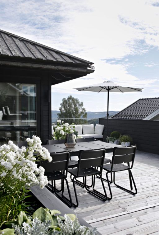 a chic terrace with a grey deck, a black built-in bench with white upholstery, a black dining set and white blooms