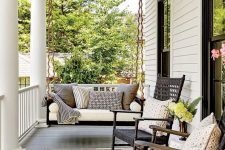 a chic vintage-inspired black and white porch with a black hanging bench with neutral upholstery, black wicker rockers and printed pillows