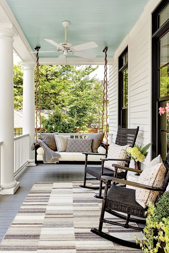 a chic vintage inspired black and white porch with a black hanging bench with neutral upholstery, black wicker rockers and printed pillows