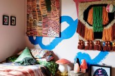a colorful kid’s room with bold blue and burgundy graffiti on the wall, a bed with colorful bedding, a woven hanging and a bold artwork