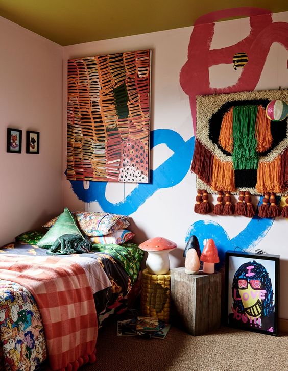 a colorful kid's room with bold blue and burgundy graffiti on the wall, a bed with colorful bedding, a woven hanging and a bold artwork