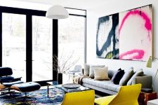 a colorful living room with a grey sofa, colorful pillows, a black chair, yellow chairs, a bold rug and a large graffiti artwork