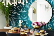 a colorful living room with a teal graffiti wall, a round mirror, a stained table and black and stained chairs, a chic chandelier