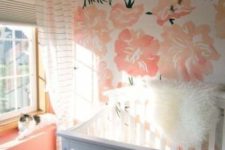 a colorful nursery with a floral statement wall, coral walls, a grey crib and white textiles to refresh the space