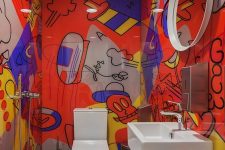 a colorful powder room with bold graffiti on the walls and white appliances, a round mirror and stainless steel touches