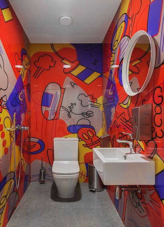 a colorful powder room with bold graffiti on the walls and white appliances, a round mirror and stainless steel touches