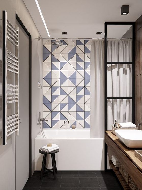 a contemporary bathroom with a blue geo tile wall in the bathtub space, black fixtures, a wooden vanity and white appliances