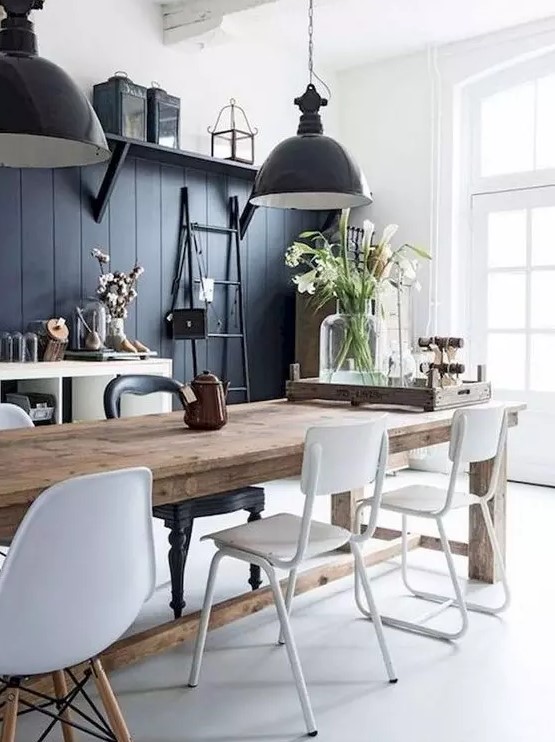 a contrasting monochromatic dining area with a black wall, a wooden table, white chairs, black pendant lamps