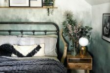 a cozy attic bedroom with green watercolor ombre walls, a metal bed with printed bedding, a ledge with potted plants and art