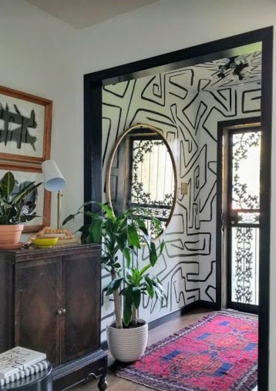 a creative entryway with a graffiti nook, a bold rug, a dark stained dresser, a round mirror and potted plants is wow