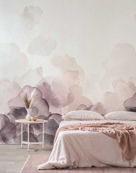 a delicate bedroom with a blush and lilac watercolor wall, a bed with blush bedding, a side table and grass in a vase