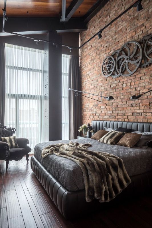 a fab industrial sleeping space with an attic ceiling, a brick accent wall, a wheel decoration on the wall, a leather bed and a refined chair