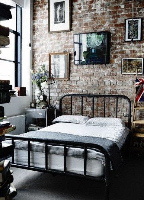 a laconic industrial bedroom with brick walls, a metal bed, mismatching nightstands, a gallery wall and vintage decor