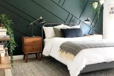 a mid-centiry modern bedroom with a dark green geometric panel wall, a metal bed, wooden furniture and some greenery in pots to enliven it