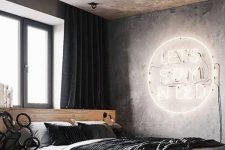 a modern industrial bedroom with a concrete ceiling and walls, a neon light, a platformbed and dark textiles