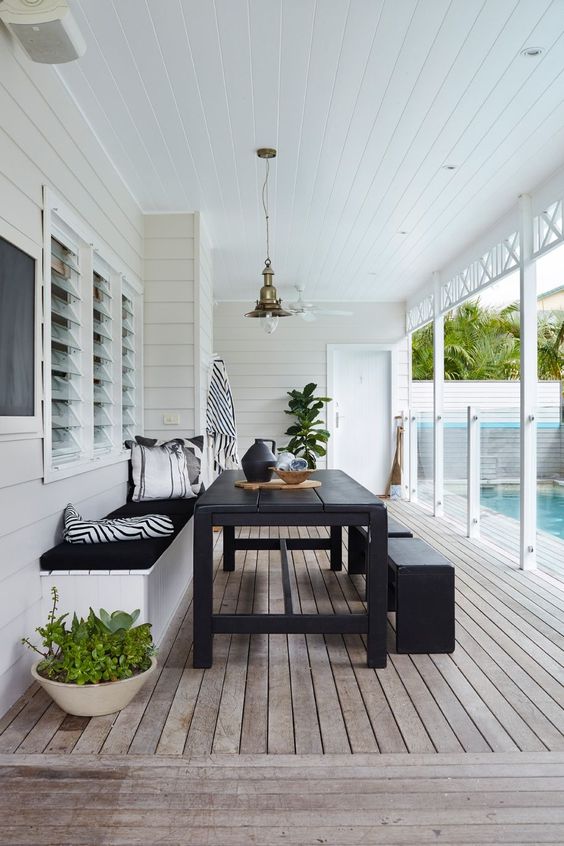 a modern terrace with a reclaimed wooden deck, a built-in bench, black dining table and benches and greenery
