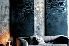 a moody industrial living room with concrete walls, black graffiti panels, a grey sofa, a bold printed rug and a chic contemporary lamp