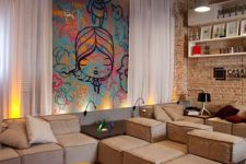 a neutral and welcoming living room with brick walls, beige low sofas, a yellow coffee table, a bold graffiti wall accent