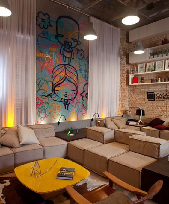 a neutral and welcoming living room with brick walls, beige low sofas, a yellow coffee table, a bold graffiti wall accent