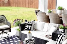 a patio with black wicker chair and black and white upholstery and a black and white printed stool plus blooms