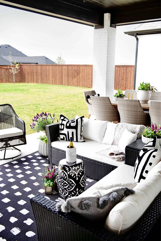 a patio with black wicker chair and black and white upholstery and a black and white printed stool plus blooms