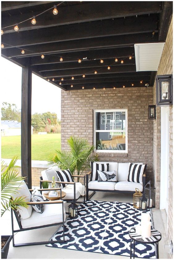a pretty black and white patio with a printed rug, black furniture with white upholstery and potted greenery and candle lanterns