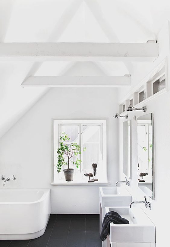 a pure hwite attic bathroom with a black tile floor, two sinks and a curved bathtub