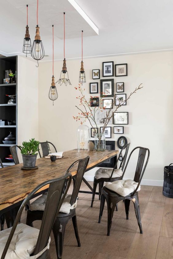 a rustic industrial dining space with a metal and wood table, metal chairs, pendant bulbs and a cool gallery wall over the fireplace