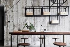 a rustic industrial home office with a large wooden desk and stools attached, exposed piping and a shelving unit