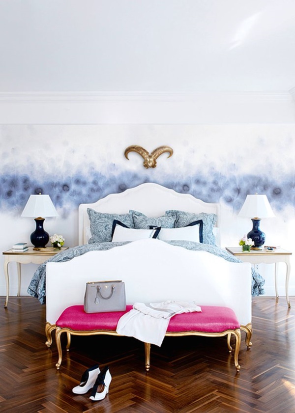 a sophisticated bedroom with a grey watercolor wall, a white bed with blue bedding, a hot pink upholstered bench, refined nightstands and table lamps