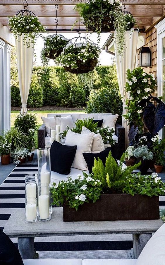a stunning black and white terrace with black wicker furniture, a stone bench, lots of greenery, blooms and candles