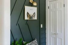 a stylish modern entryway with a black paneled wall, a small bench, a sconce and potted greenery is very cool