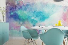 a super bold dining room with a bright watercolor accent wall, a round table and blue chairs, a blue storage unit and pendant lamps
