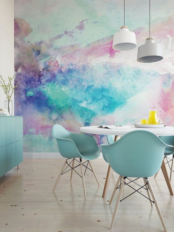 a super bold dining room with a bright watercolor accent wall, a round table and blue chairs, a blue storage unit and pendant lamps