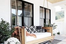a terrace with a black and white rug, a hanging bench and printed pillows and potted greenery and blooms