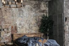 a vintage industrial bedroom with shabby brick walls and a ceiling, a wooden bed and a storage unit, shutters for decor and an industrial chandelier