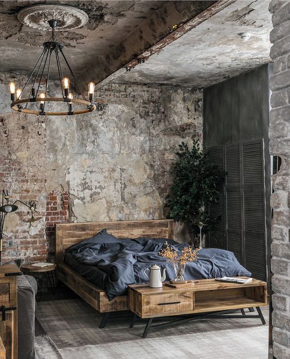 a vintage industrial bedroom with shabby brick walls and a ceiling, a wooden bed and a storage unit, shutters for decor and an industrial chandelier