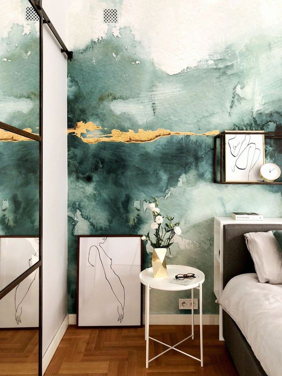 an eye catchy bedroom with a green watercolor wall with touches of gold, a bed with neutral bedding, artwork, a side table