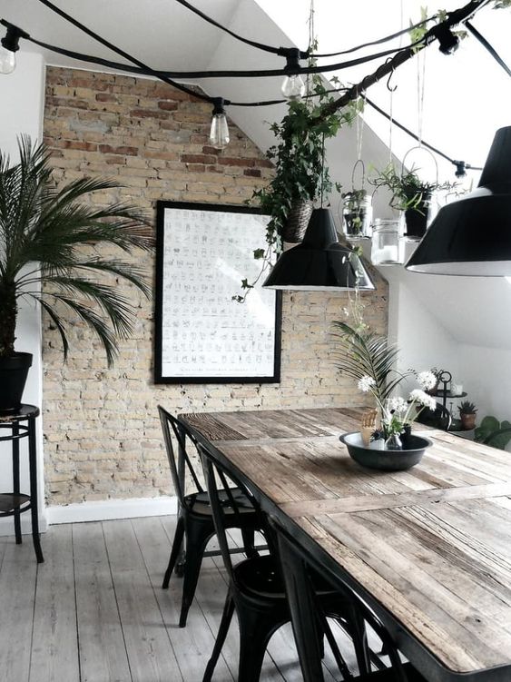 an industrial Scandinavian space with a brick accent wall, a wooden dining table, black metal chairs, string lights and black metal lampshades