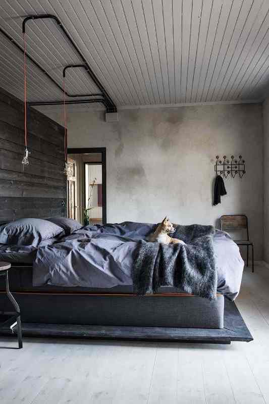 an industrial bedroom with a planked ceiling, concrete walls, a reclaimed wood accent wall, an upholstered bed with grey bedding