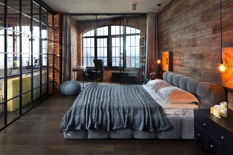 an industrial bedroom with a wood clad accent wall, an upholstered bed, a home office space by the window, a desk and a black chair, glass doors