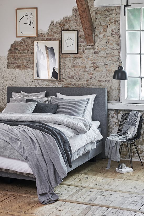 an industrial bedroom with shabby chic brick walls, an upholstered bed with neutral bedding, a pendant lamp and a gallery wall