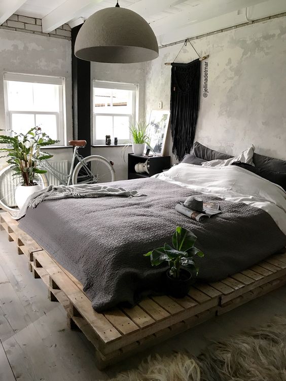 an industrial bedroom with shabby chic walls, a pallet bed with black and white bedding, a bike and a pendant lamp