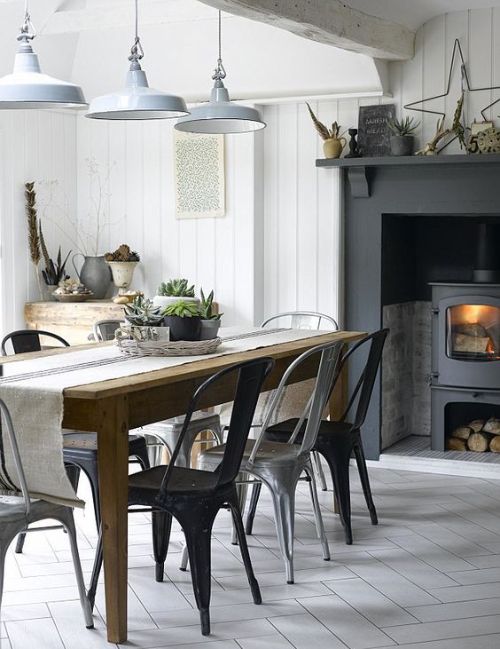 an industrial cottage kitchen with a hearth with a large mantel, a wooden dining table, metal chairs and white metal pendant lamps