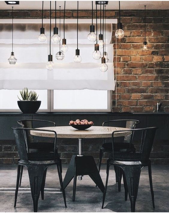 an industrial dining room with brick walls, a round table, black chairs, pendant bulbs and a potted plant is amazing