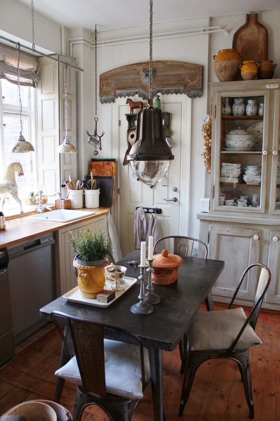 an industrial dining space right in the kitchen, with a black metal table and chairs, metal pendant lamps and potted plants