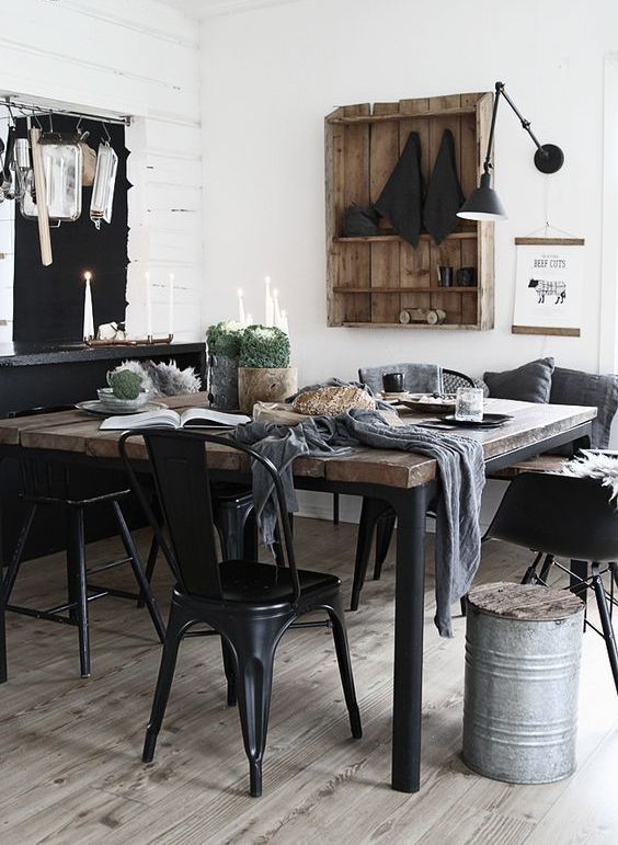 an industrial dining space with a black credenza, a minimal wood and metal table, black metal chairs and a black sconce